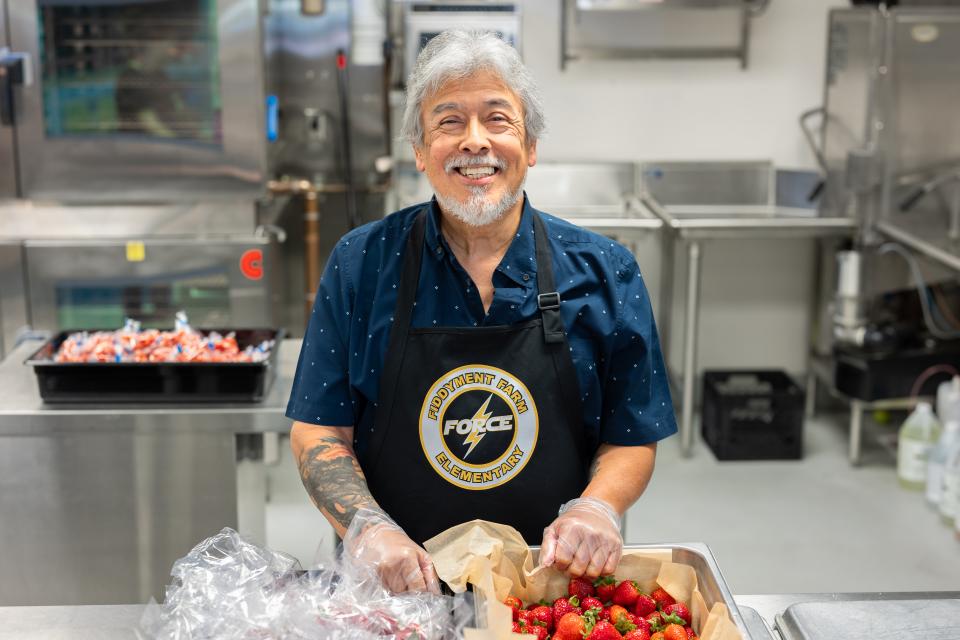 Cafeteria staff standing in school kitchen, smiling in front of a tray of strawberries. 